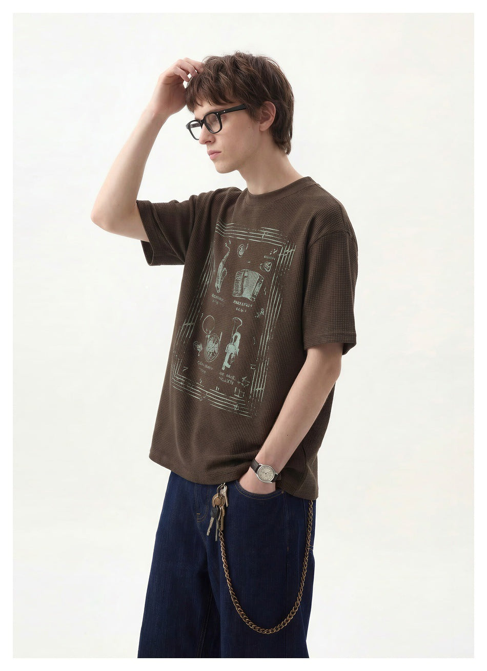 Model wearing a dark brown waffle-textured short-sleeve T-shirt with a large pale graphic on the front.