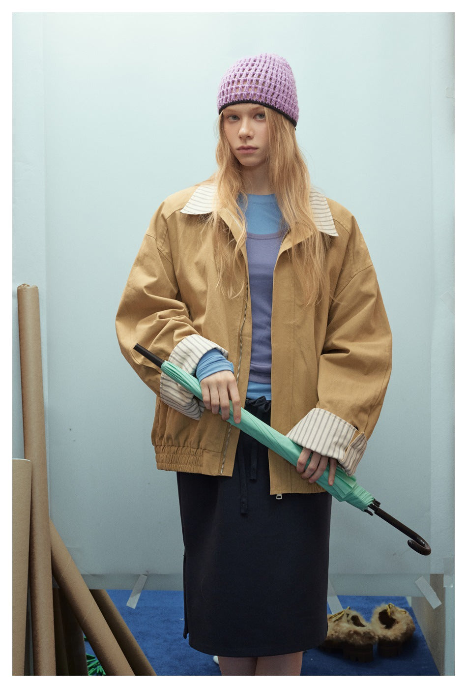 Front view of a model wearing an oversized tan jacket with striped collar and cuffs.