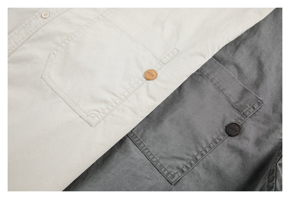 Close-up of two shirts in off-white and charcoal, showing chest pockets with stitched edges and small buttons.