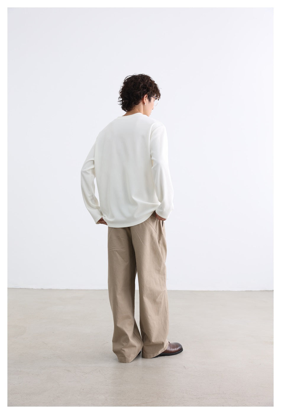 Rear view of a model wearing an ivory long-sleeve top and loose beige trousers.