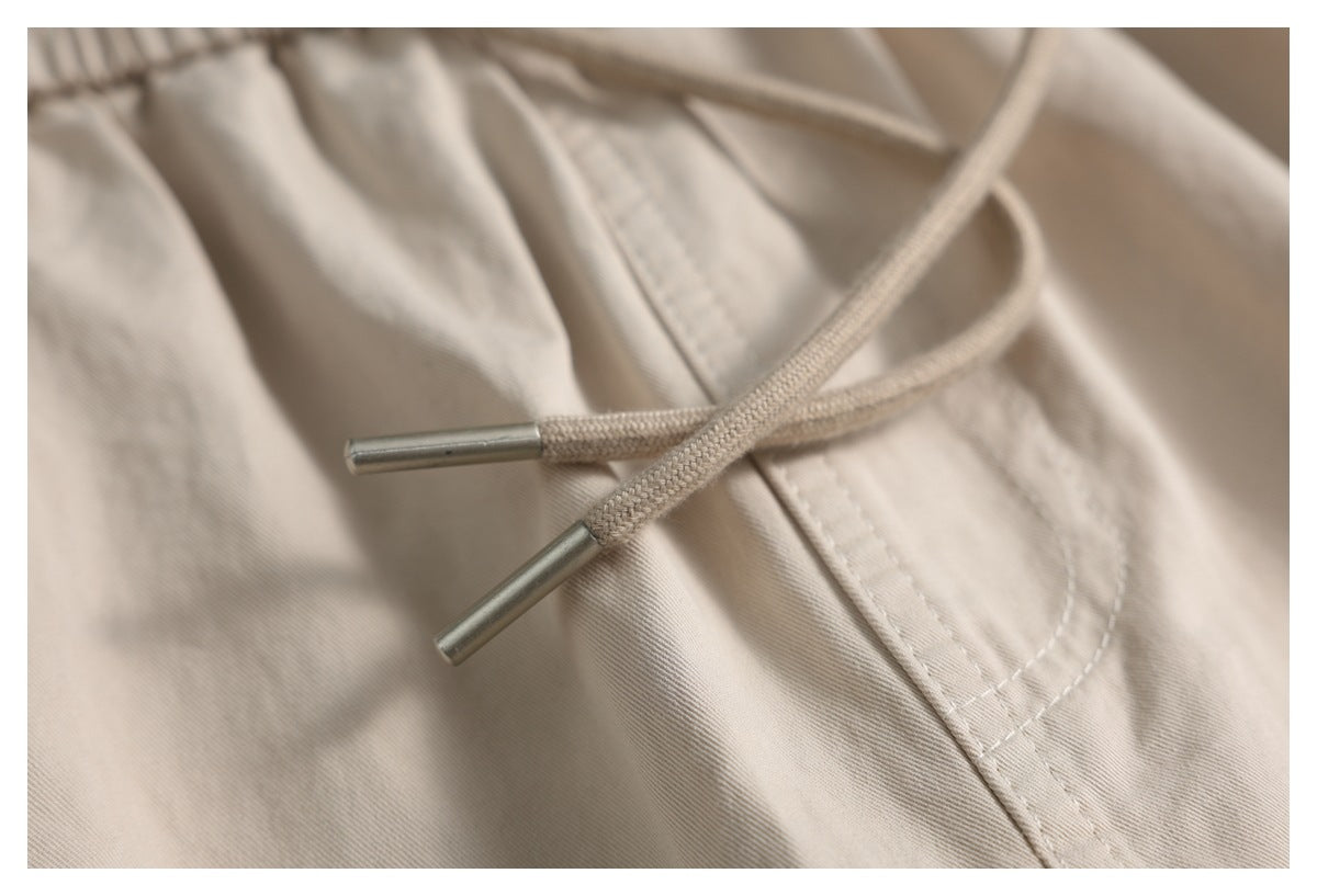Close-up of beige trouser drawcords with metal tips over a stitched pocket area.