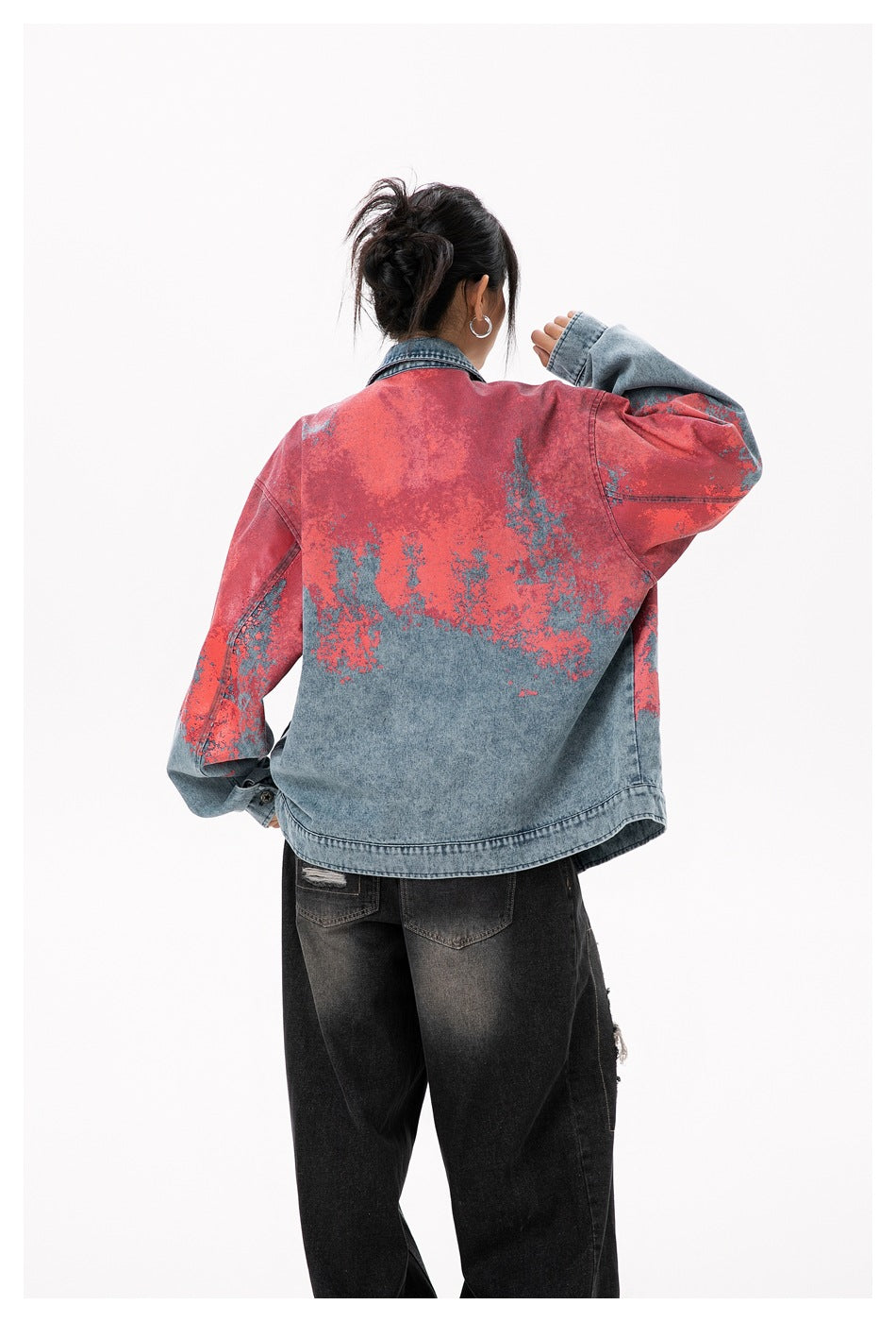 Back view of a model wearing an oversized blue denim jacket with coral-red and blue mottled detailing.