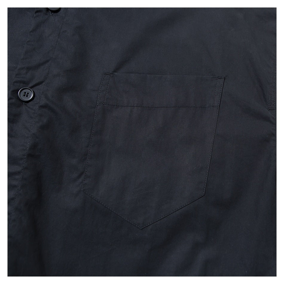 Close-up of a black garment showing a large stitched patch pocket and a black button on the placket.
