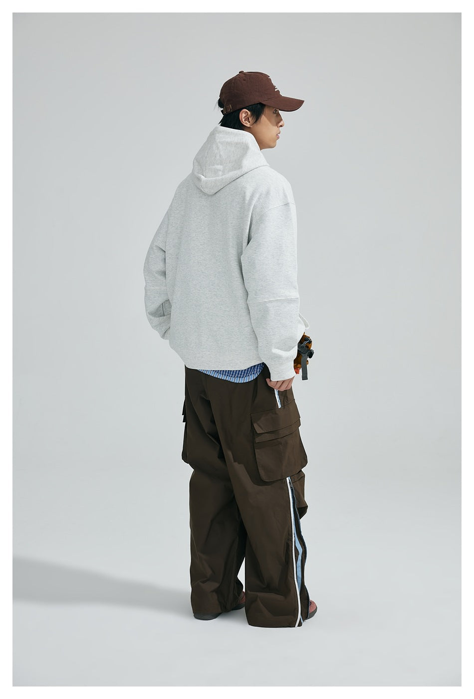 Rear view of a model wearing a light gray hooded sweatshirt with loose sleeves and a plain back.