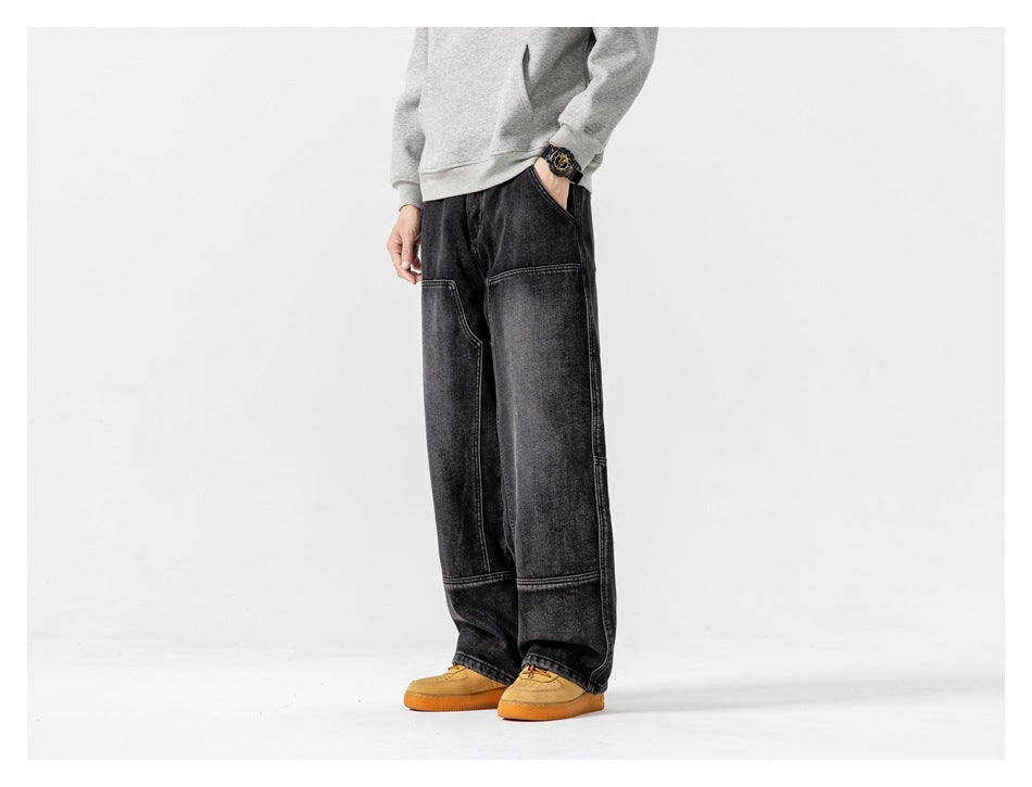 Three-quarter front view of a model wearing loose black washed jeans with prominent panel seams.