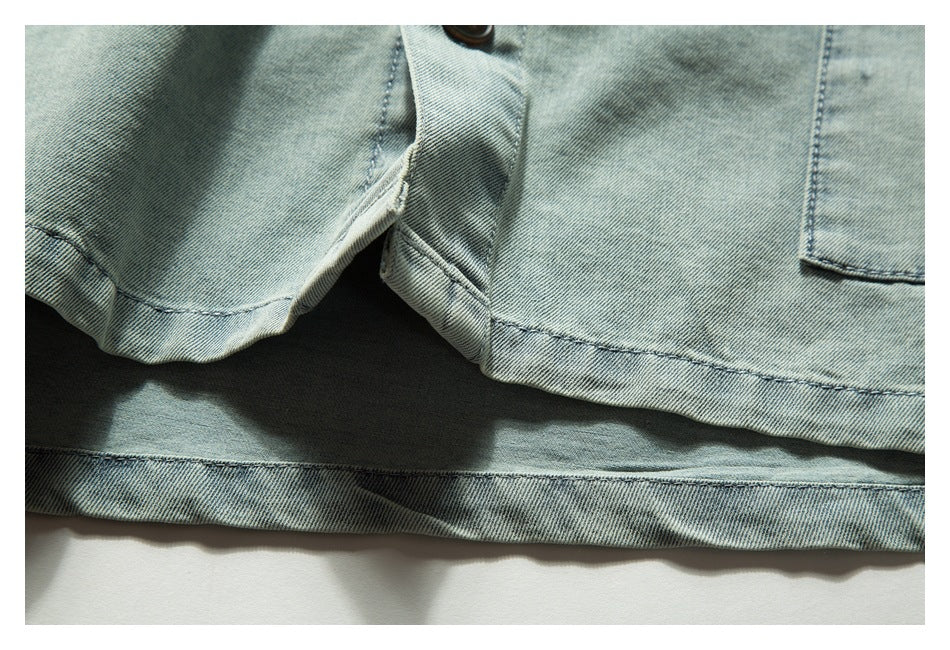 Close-up of light blue denim with a button, overlapping seam, and stitched hem.