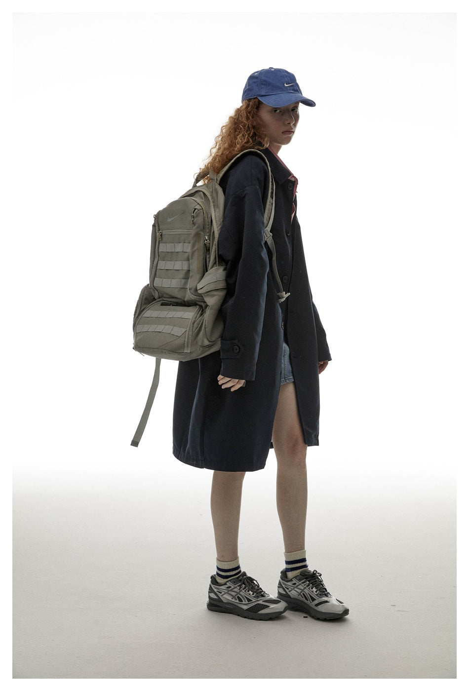 Model in a dark long coat, shown in side view with a large gray backpack.