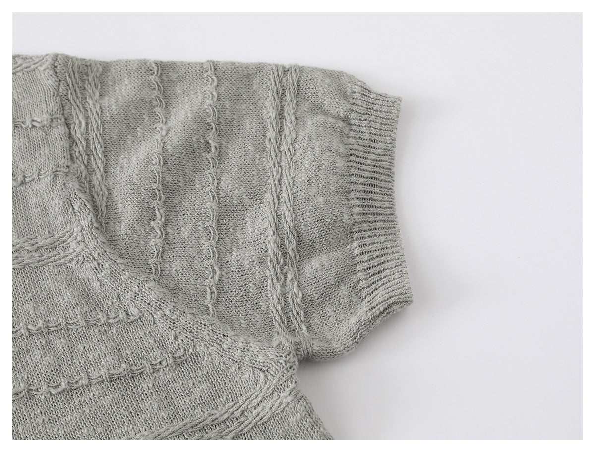 Close-up of a light gray knitted sleeve and ribbed cuff with raised decorative stitch bands.