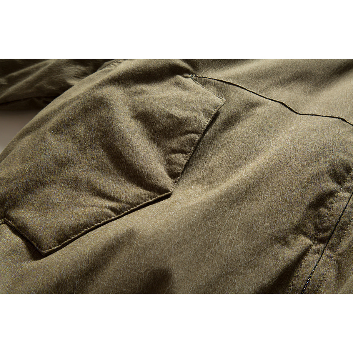 Close-up of an olive-brown jacket's flap pocket, stitching, and front zipper.