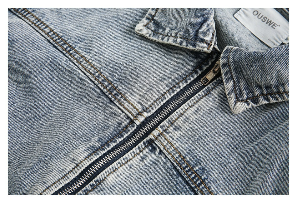 Close-up of the metal front zipper, collar, and stitching on a light-wash denim jacket.
