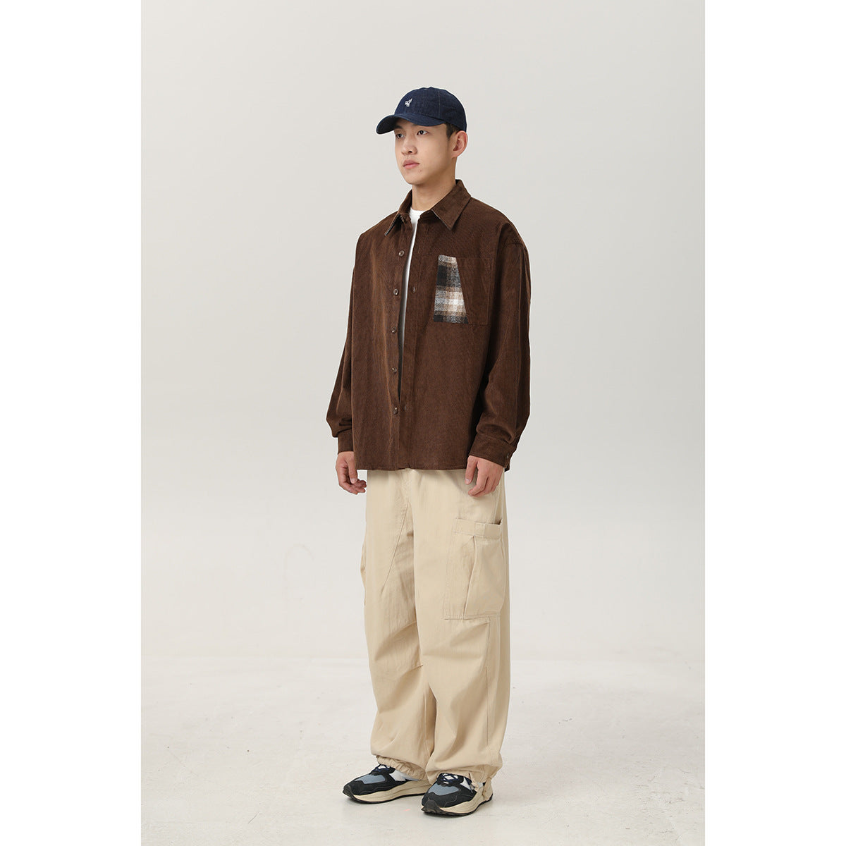Full-length view of a model wearing a brown plaid-pocket shirt, loose cream cargo pants, and a navy cap.