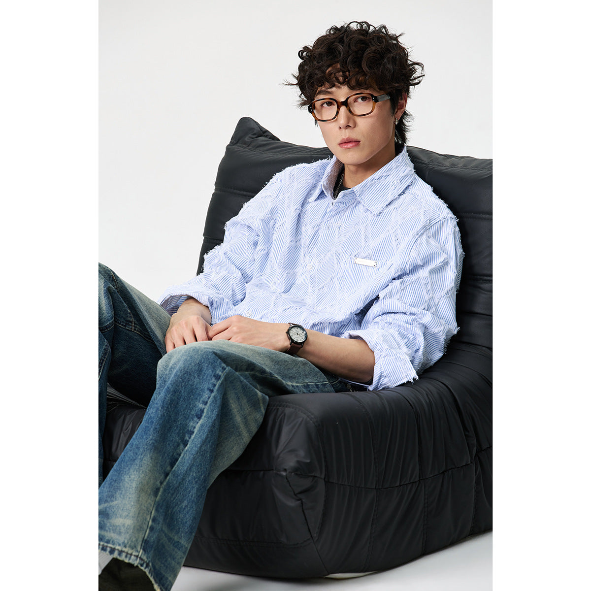 Model seated in a black chair wearing a pale blue pinstriped shirt with raised white diamond detailing.