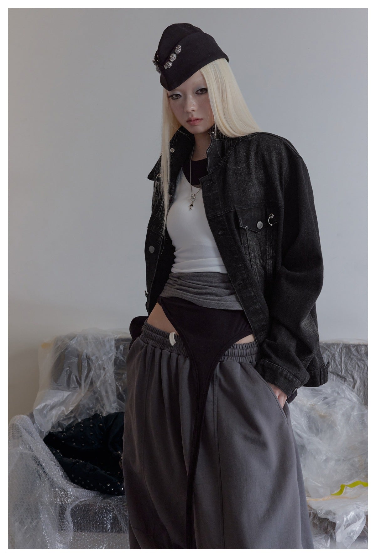 Model wearing an oversized black denim jacket with silver hardware over a white top and dark bottoms.