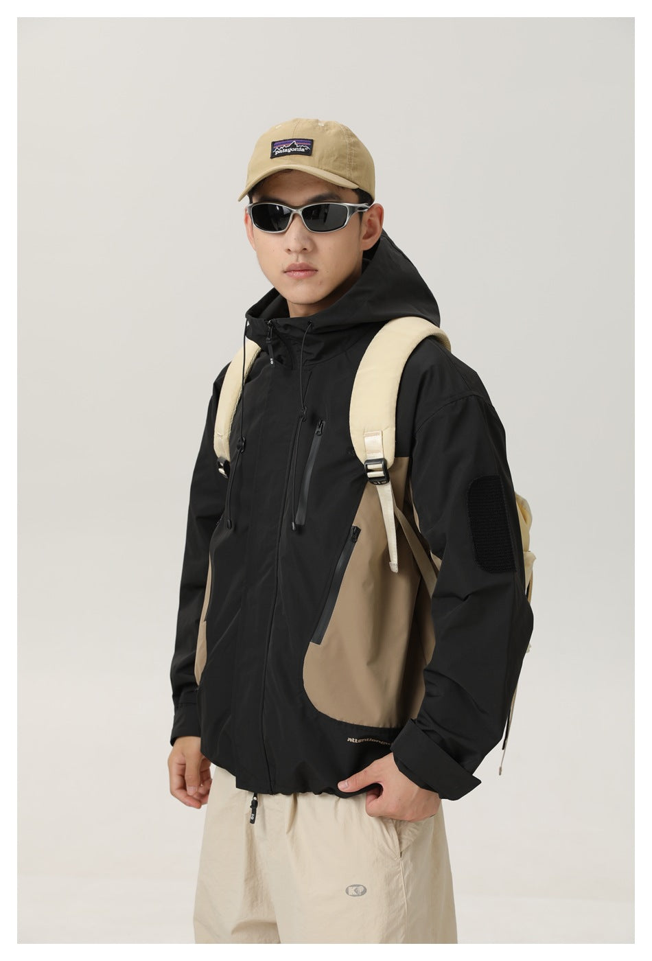 Closer front view of a black and tan hooded jacket with zip pockets and a sleeve patch, worn by a model.