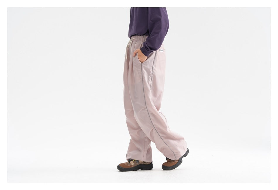 Side view of a model wearing loose pale pink trousers with an elastic drawstring waist and side pocket.
