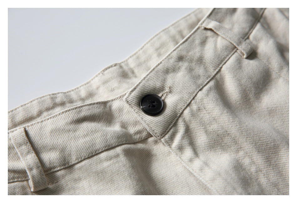 Close-up of light beige trousers showing the waistband, belt loop, and black button.
