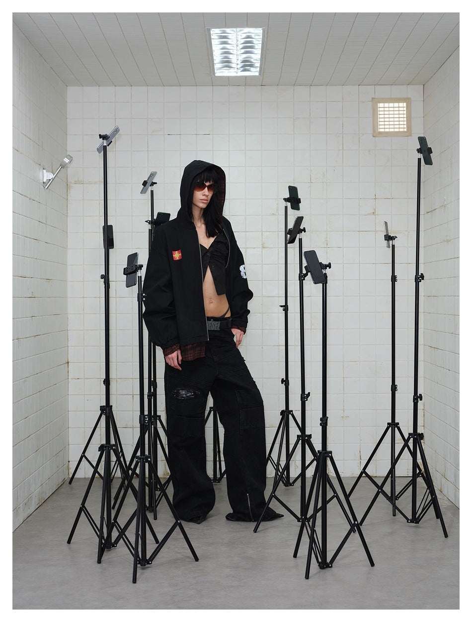 Model in a black hooded jacket with plaid hem, worn open over a black top and wide black pants