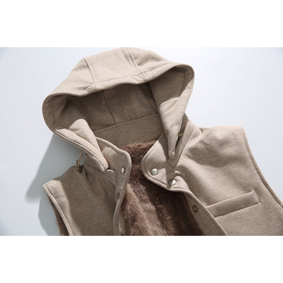 Close-up of a beige hooded vest with snap buttons and brown plush lining.