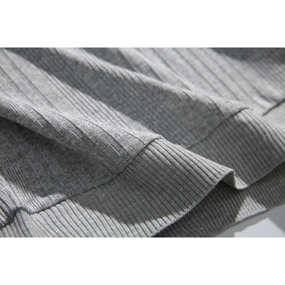 Close-up of the ribbed knit texture and hem edge of a light gray polo shirt.