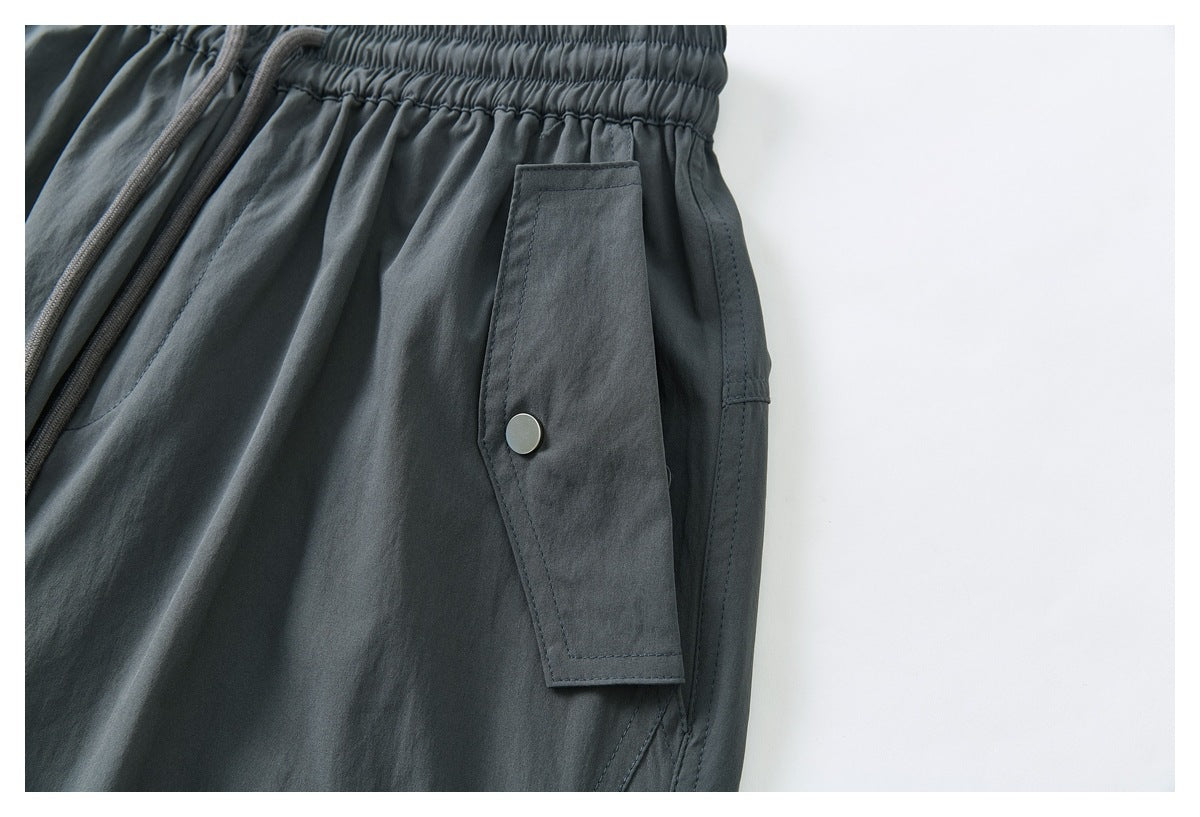 Close-up of a snap-button flap pocket and elastic waistband on dark charcoal cargo pants.
