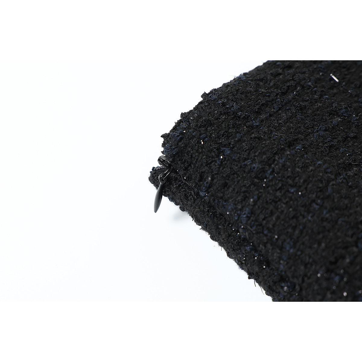 Close-up of a black zipper and pull along the edge of textured black fabric.