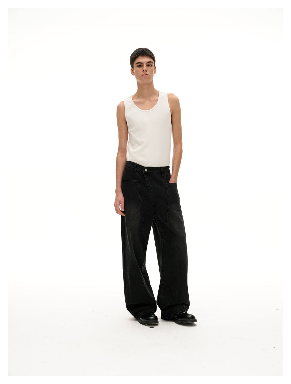 Front view of a model in a white tank top and wide black jeans, one hand in a pocket.