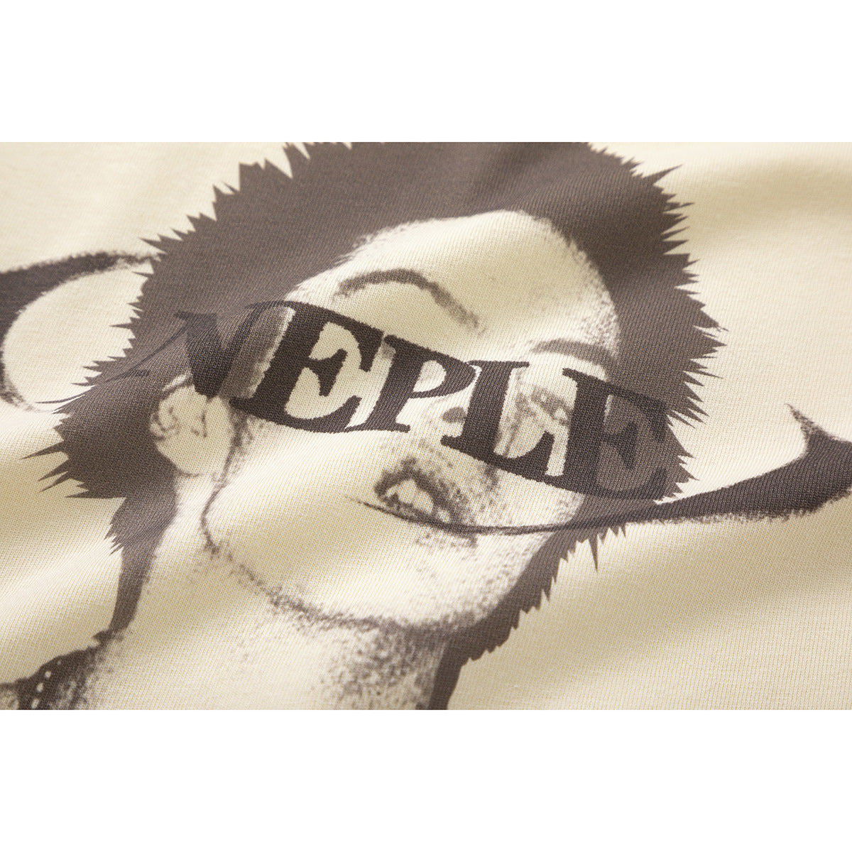 Close-up of a monochrome portrait graphic with bold lettering printed on cream T-shirt fabric.