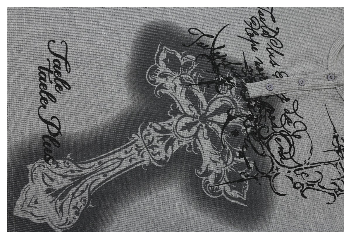 Close-up of a gray waffle-knit top showing its button placket and ornate black-and-gray script print.
