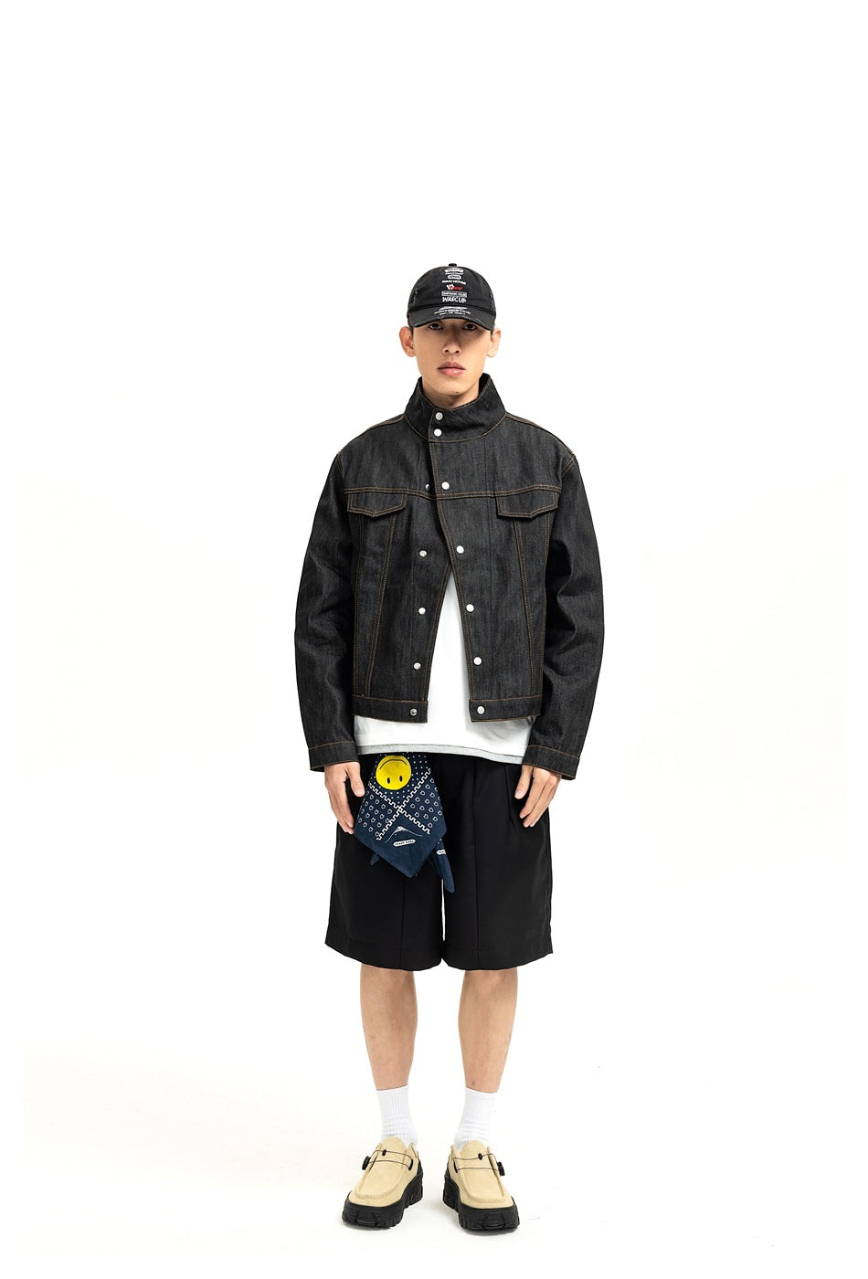 Model wearing a black denim jacket with stand collar over a white tee, black shorts, a bandana and beige shoes, front view