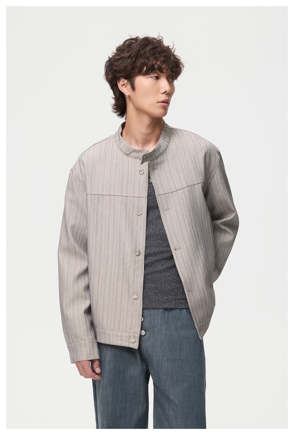 Model wearing a light gray pinstriped stand-collar jacket over a dark shirt and blue jeans.