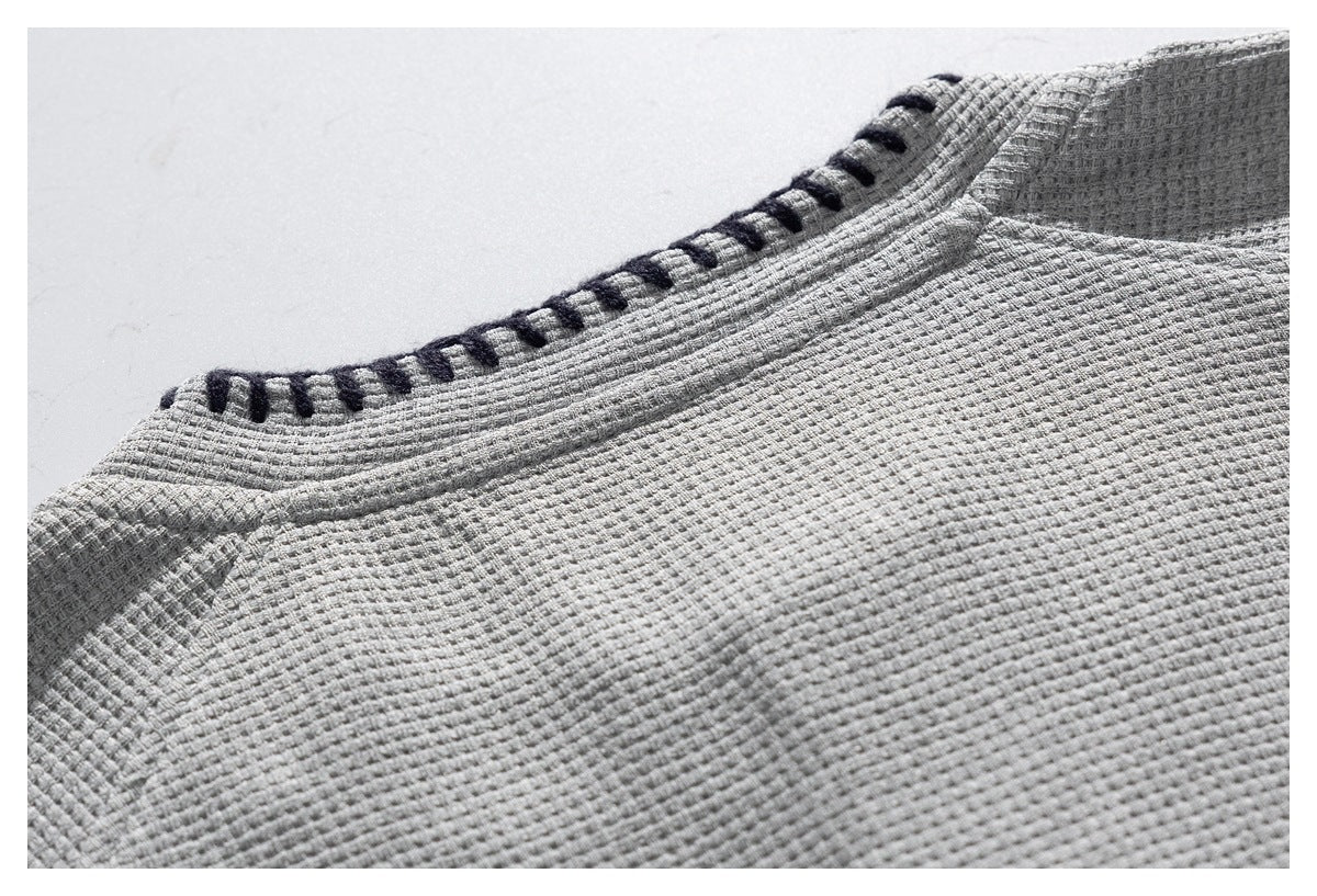 Close-up of the light gray shirt's rounded neckline with dark contrast stitching and textured fabric.