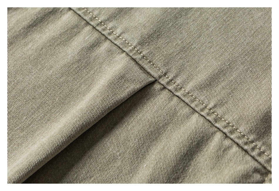 Close-up showing a folded khaki-olive garment panel and a diagonal stitched seam.