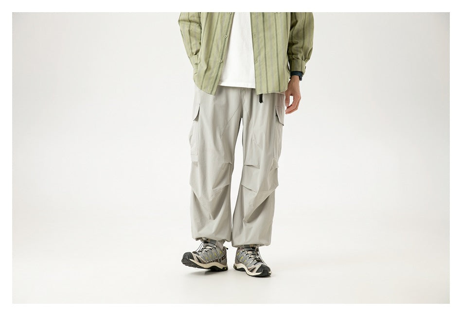 Cropped model wearing loose light gray cargo pants with layered thigh pockets and gathered ankle cuffs, front view.