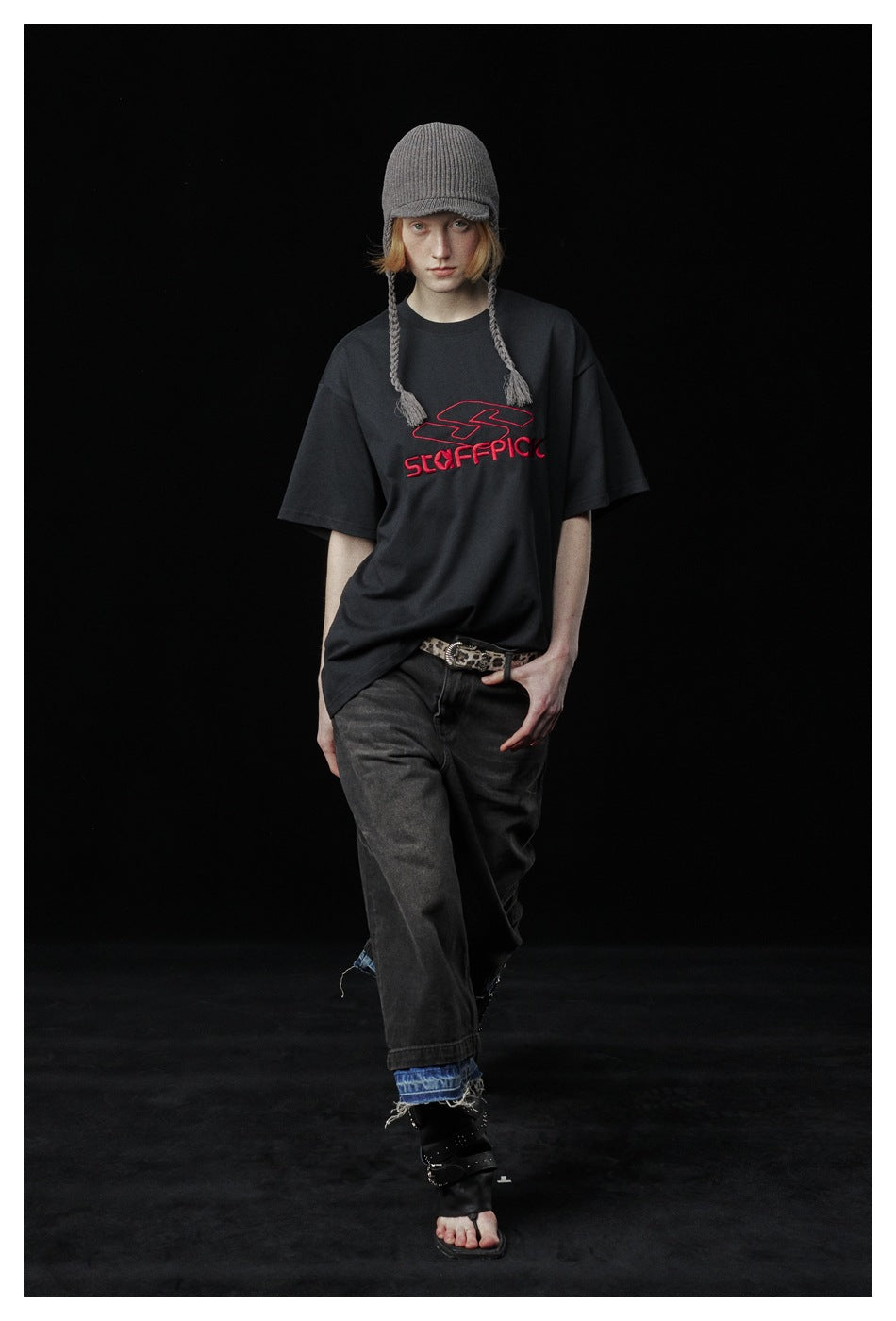 Model wearing a charcoal oversized T-shirt with a red chest graphic, dark jeans, and a gray knit hat.