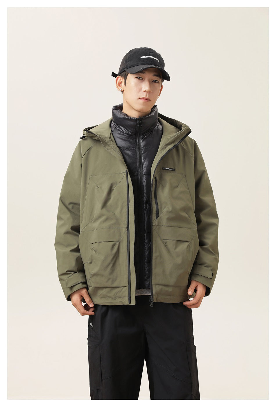 Front view of a model wearing an open olive hooded jacket over a black quilted jacket.