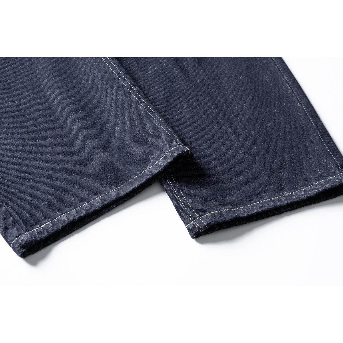 Close-up of dark indigo jeans showing two stitched hems and the lower legs.