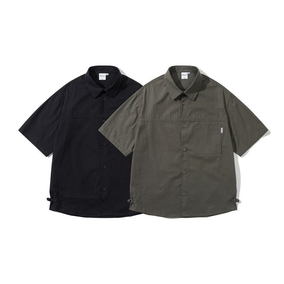 Two short-sleeve button-up shirts shown from the front in black and olive gray, each with a chest pocket and hem ties.