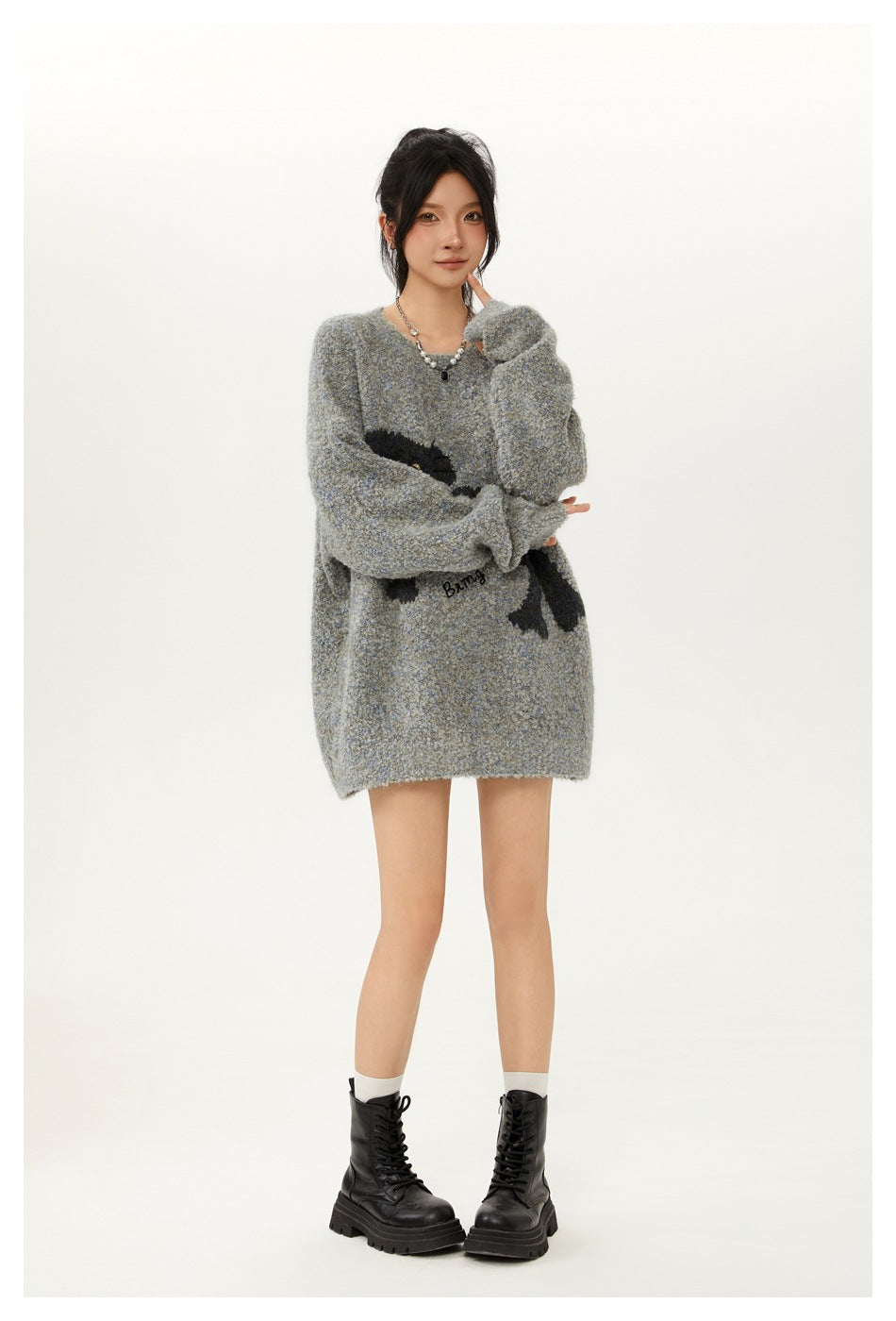 Full-length model wearing an oversized gray-blue sweater with a black cat graphic, black skirt, and lace-up boots.
