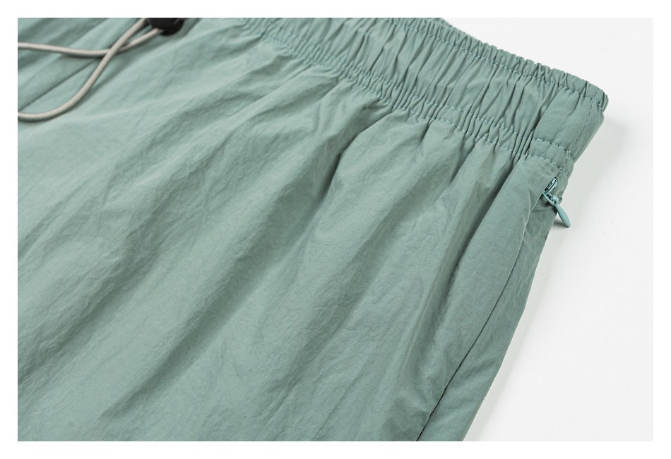 Close-up of sage green shorts showing the gathered waistband and a side pocket with a small zipper pull.