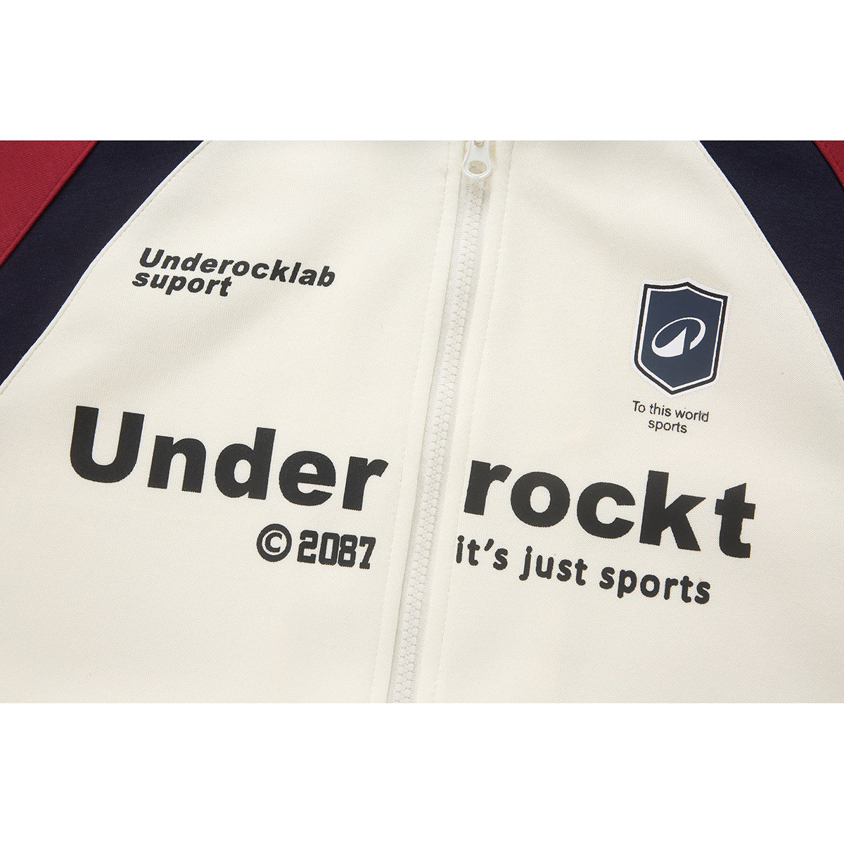 Close-up of the hoodie’s cream chest, showing a white zipper and black printed text with a shield emblem.
