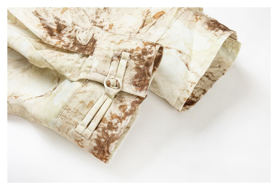 Close-up of a cream shirt sleeve cuff with a buttoned tab and brown abstract print.