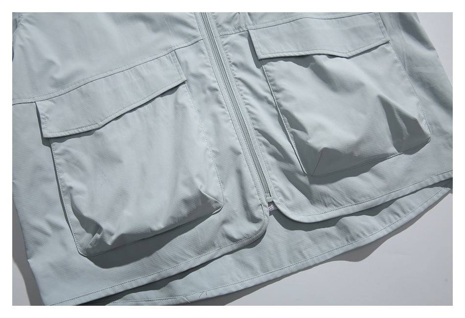 Close-up of the pale gray jacket's lower front with two large flap pockets and a central zipper.