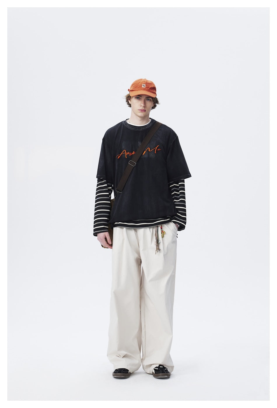 Full-length model wearing a black graphic T-shirt over a black-and-white striped long-sleeve shirt with loose white pants.