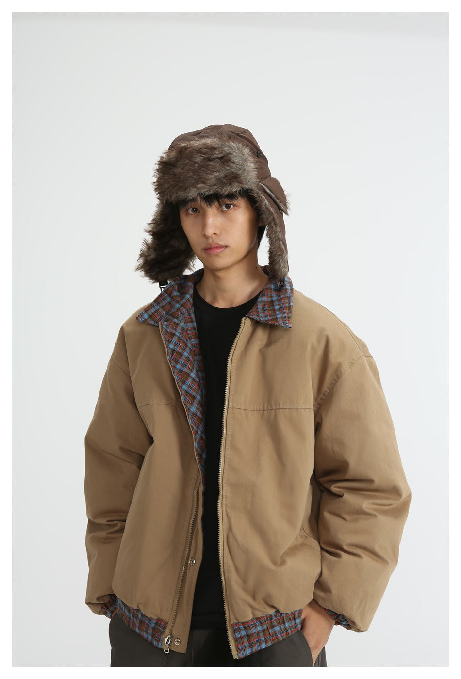 Close-up of model in open khaki jacket showing plaid interior facing, zipper and snap closure, with a fur-style hat