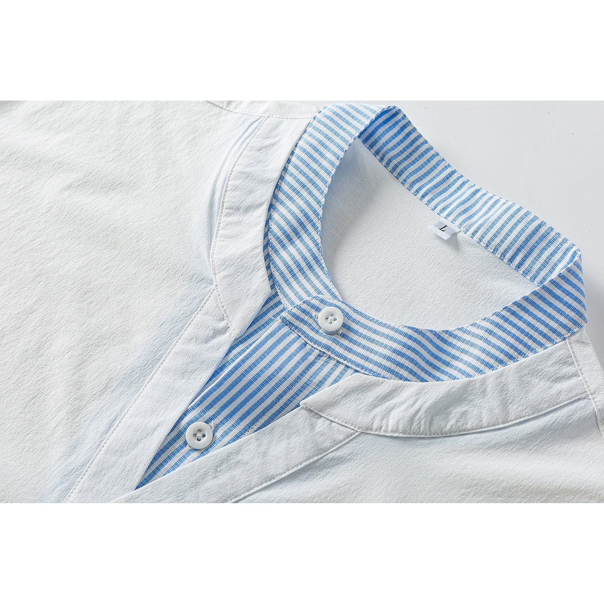 Close-up of a white shirt with a blue-and-white striped collar and placket, two white buttons, and a small size L tag.
