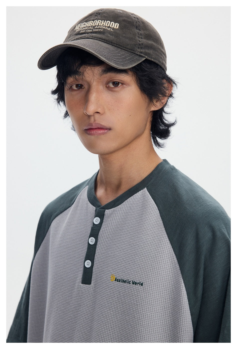 Close view of a model wearing a gray textured raglan henley with dark green sleeves and a three-button placket.
