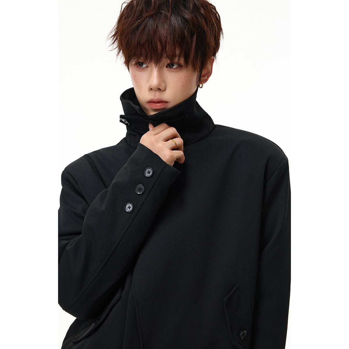 Close-up of a model wearing a black high-collar coat with three sleeve buttons.
