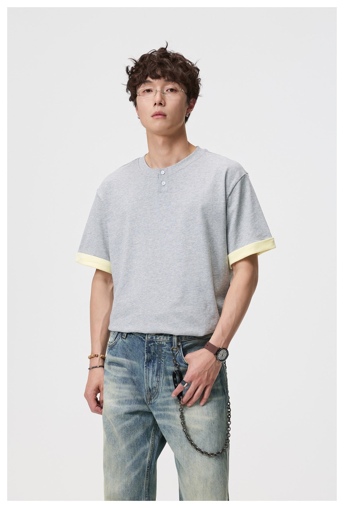 Man wearing a gray short-sleeve button-neck T-shirt with yellow cuffs and light-wash jeans, front view
