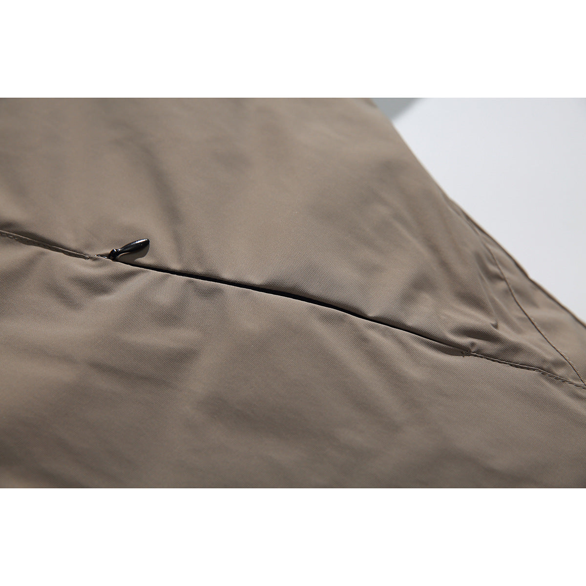 Close-up of taupe jacket fabric with a stitched seam and a small black tab.