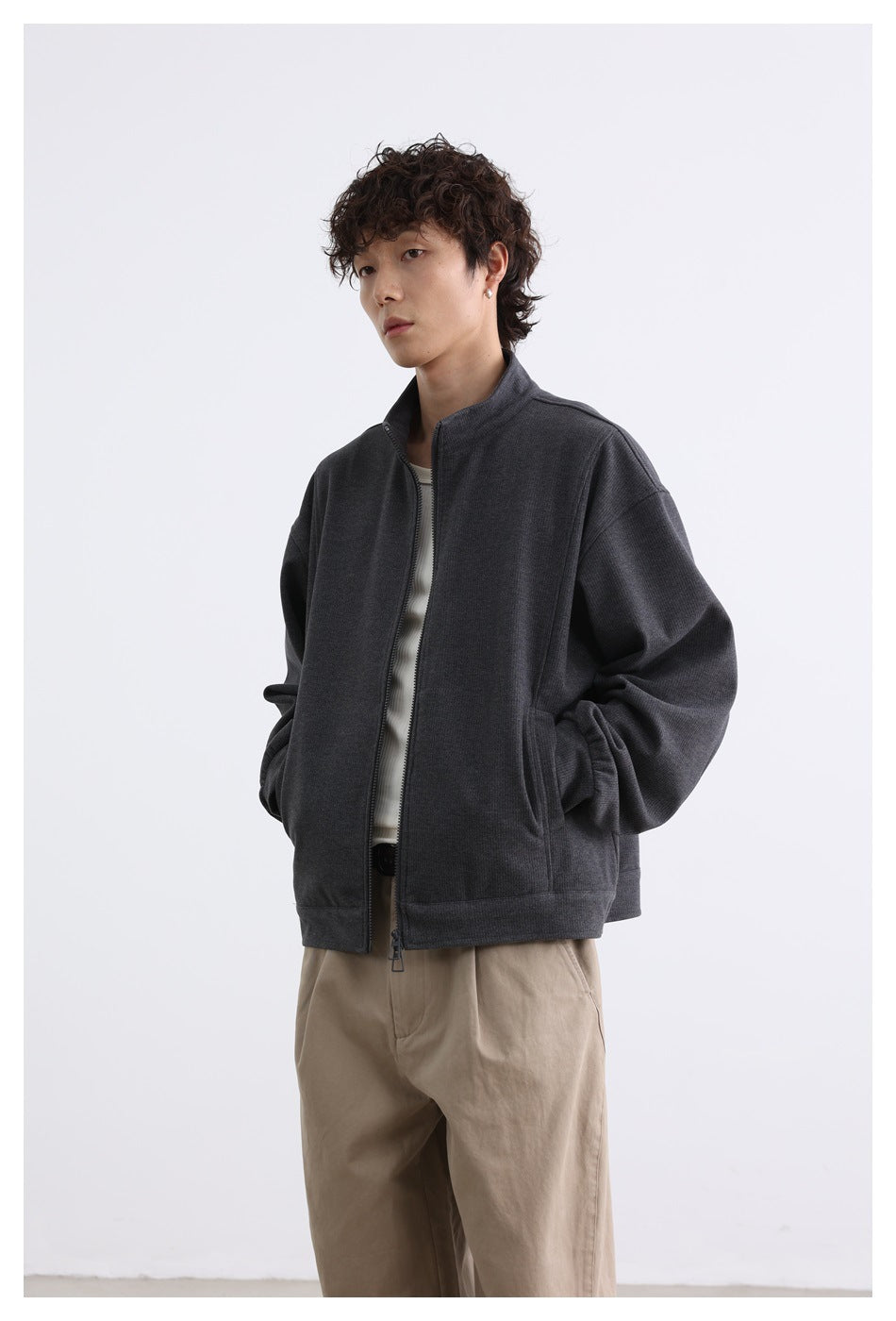 Closer angled view of a model wearing a charcoal stand-collar zip jacket over a light top.